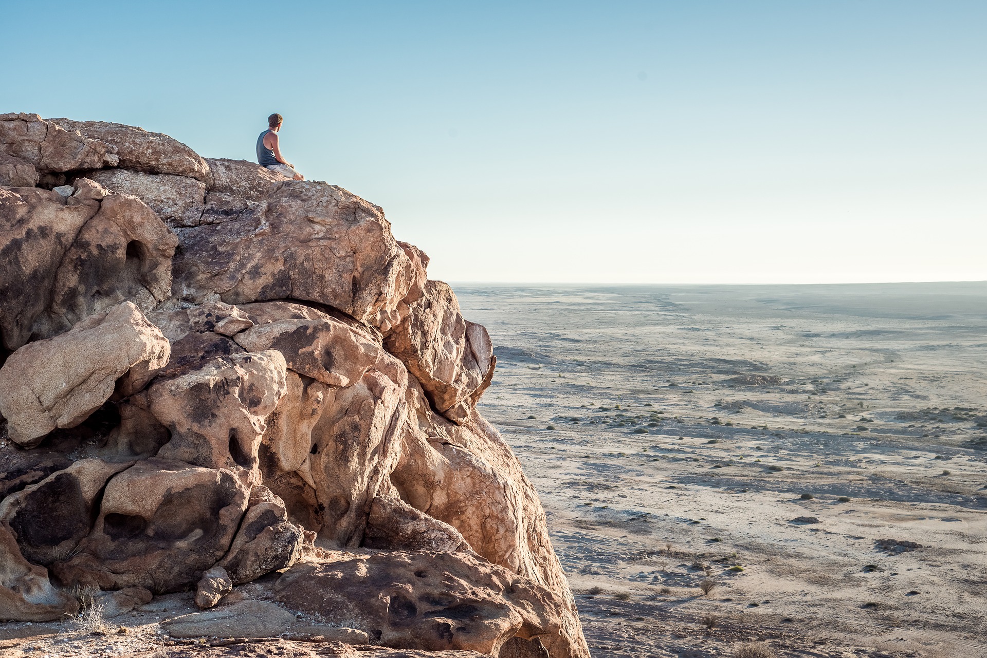 崖の上で夕日を眺めている男性の写真