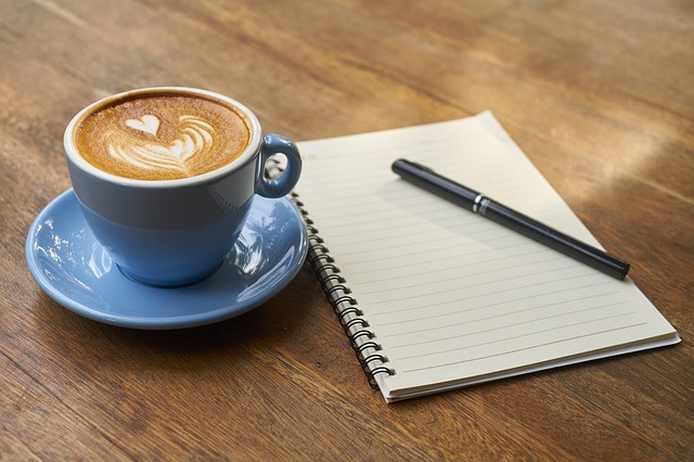 カフェ屋さんでコーヒーを片手にノートを広げて考え込んでいる様子